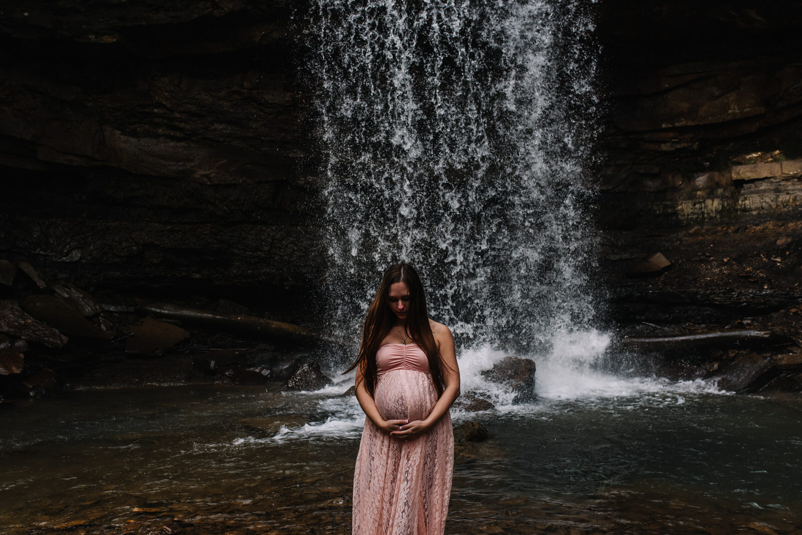  mom to be holds her belly under waterfall at cucumber falls in ohiopyle 